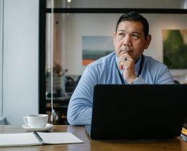 thoughtful ethnic businessman using laptop while working in office