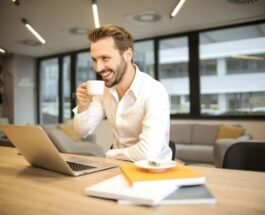depth of field photo of man sitting on chair while holding cup in front of table