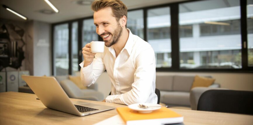 depth of field photo of man sitting on chair while holding cup in front of table