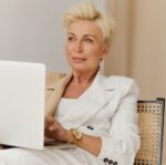 woman in white blazer holding a laptop