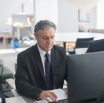 man in black suit sitting at his desk and working