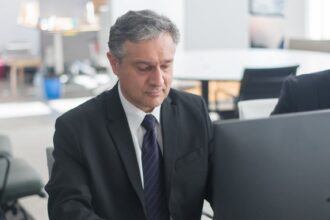 man in black suit sitting at his desk and working
