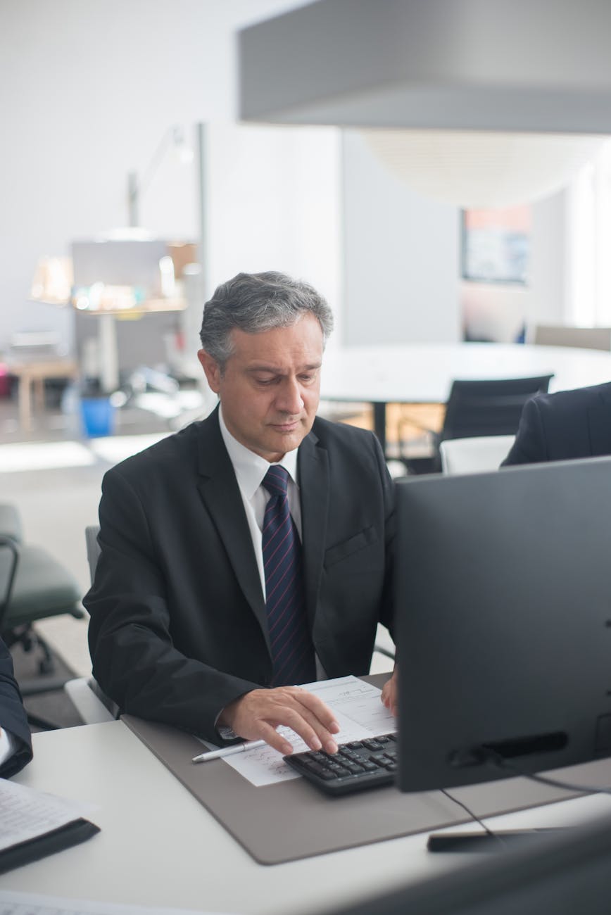 man in black suit sitting at his desk and working