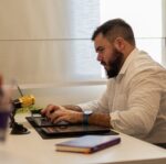 man in shirt sitting and working on laptop