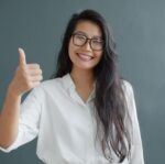 confident woman giving thumbs up in white shirt